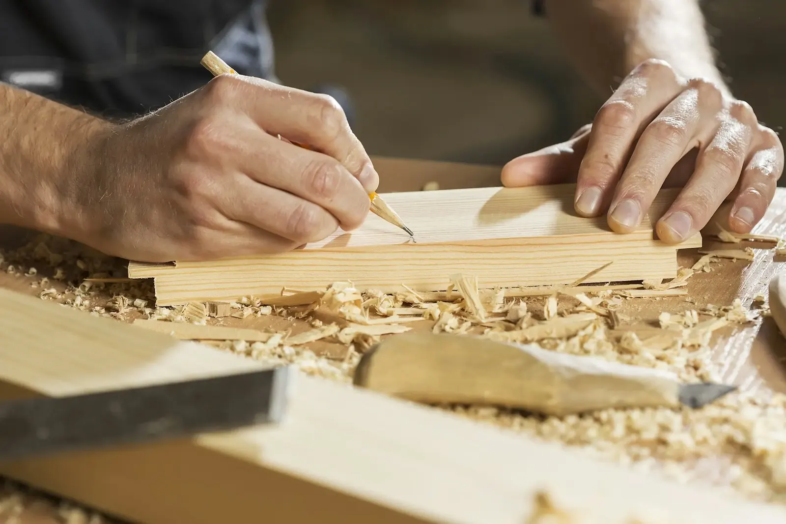Hände zeichnen mit Bleistift eine Linie auf ein Holzbrett
