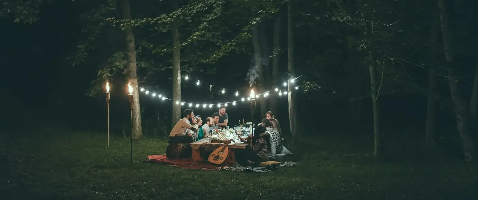 Lichterkette über einer Gruppe am Tisch im nächtlichen Wald